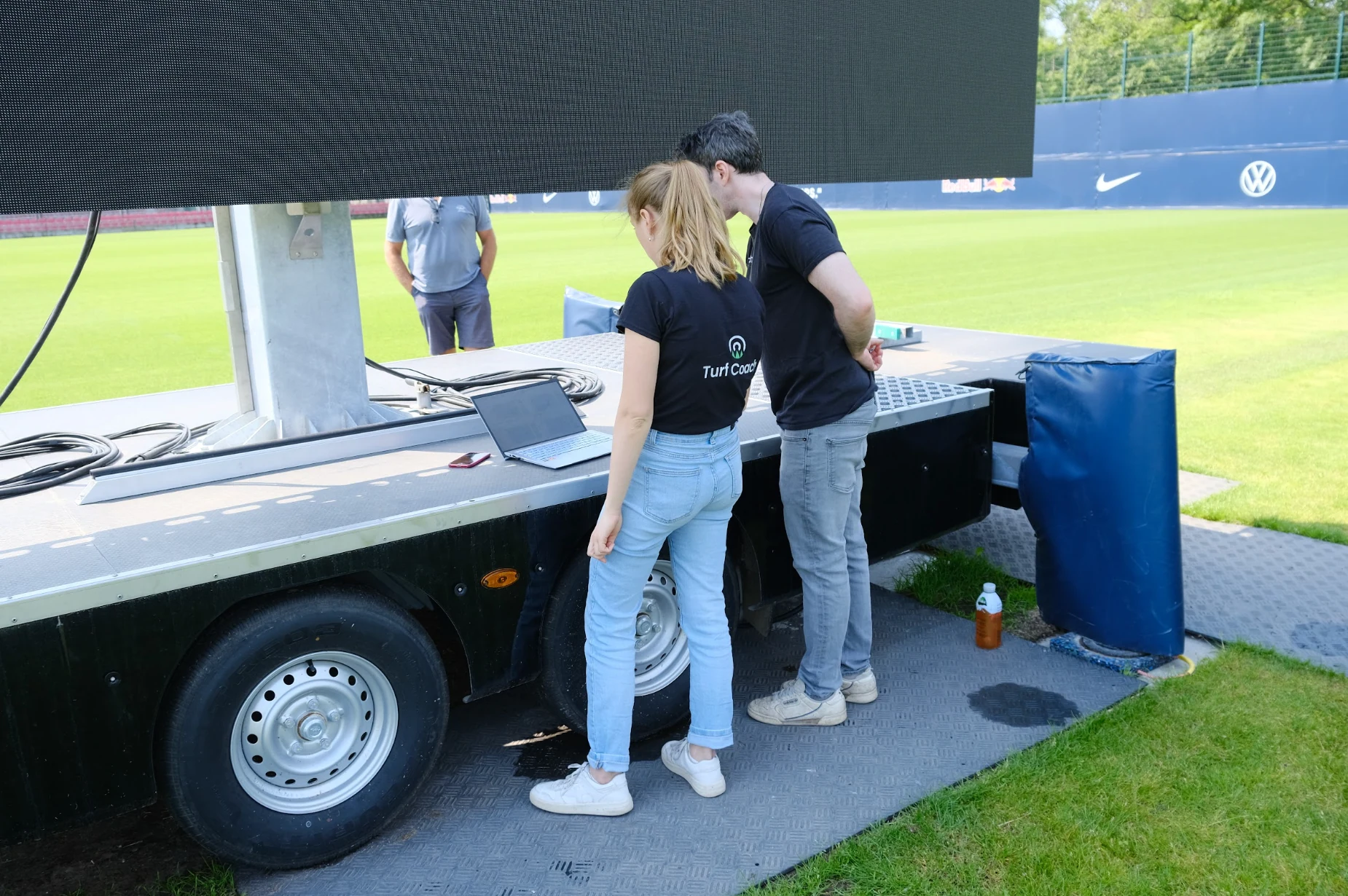 Two turfcoach team members reviewing a laptop beside a football pitch